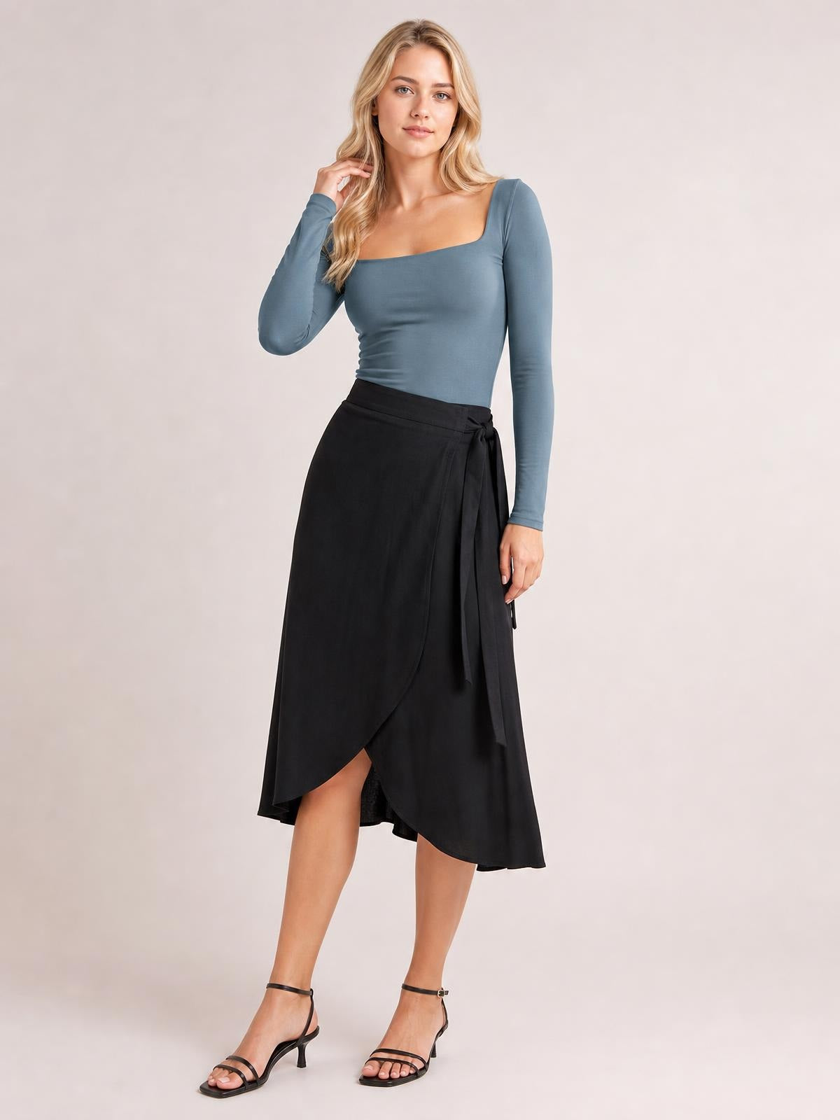 A model poses in a slate-blue square neck long sleeve T-shirt with a fitted silhouette, gently touching her hair with one hand.