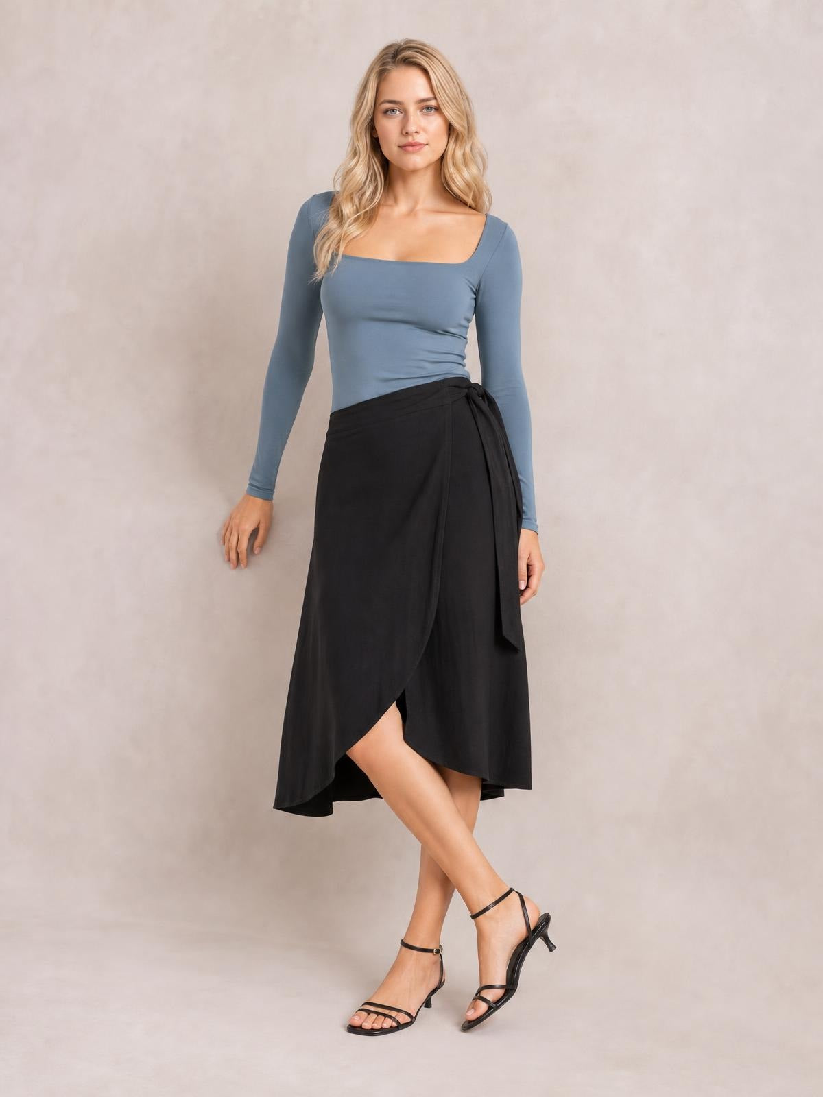 A model poses in a fitted blue square neck long sleeve T-shirt with a classic silhouette and moderate stretch, paired with a black wrap skirt.