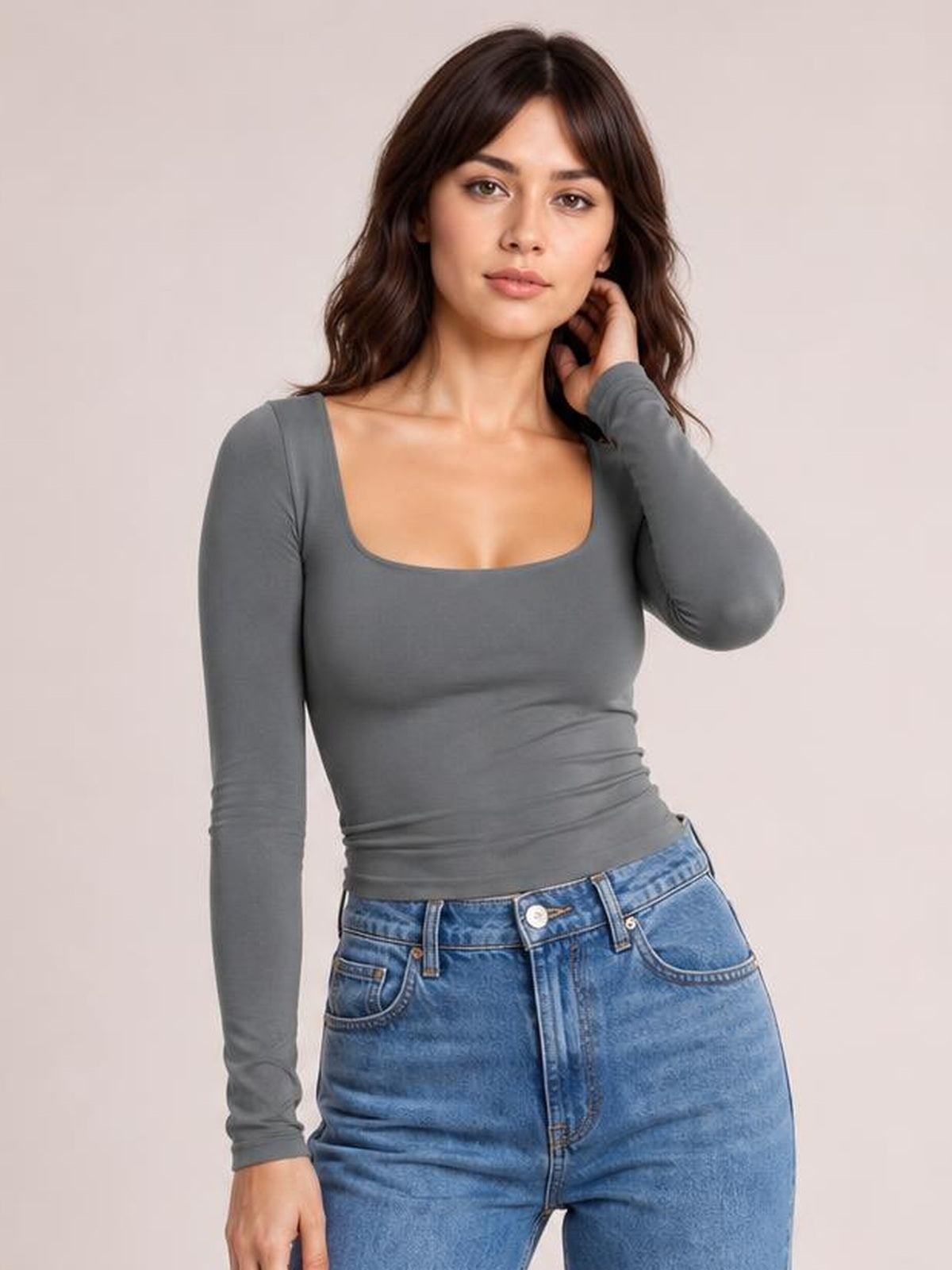Model wearing a fitted gray square neck long sleeve T-shirt with a smooth, stretchy silhouette, posing with one hand touching her hair.