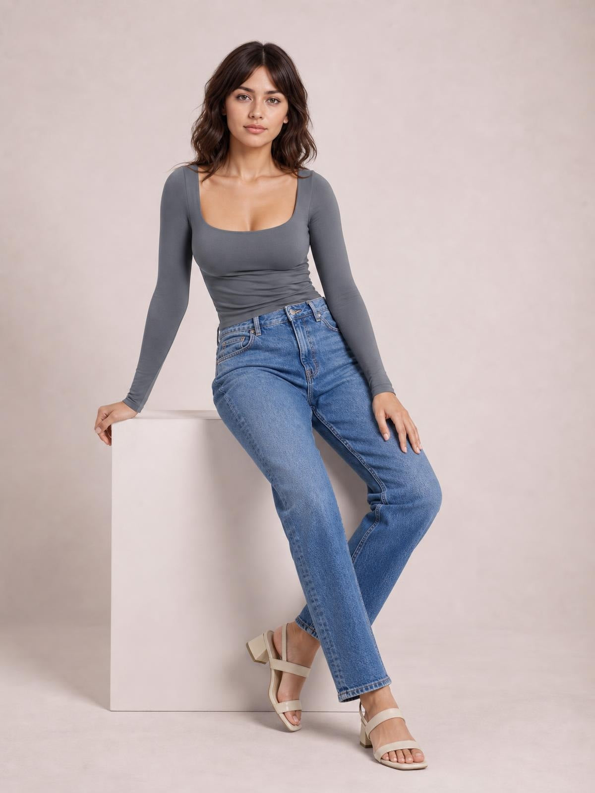Model sits with crossed legs wearing a fitted gray square neck long sleeve T-shirt, featuring a basic silhouette and softly gathered waist.