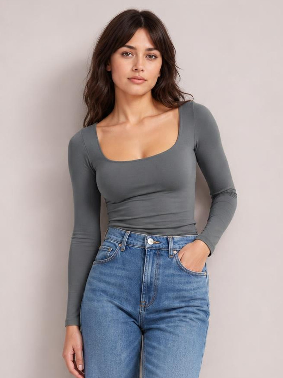 Model wearing a gray square neck long sleeve T-shirt with a fitted silhouette, paired with blue jeans and one hand in a pocket.