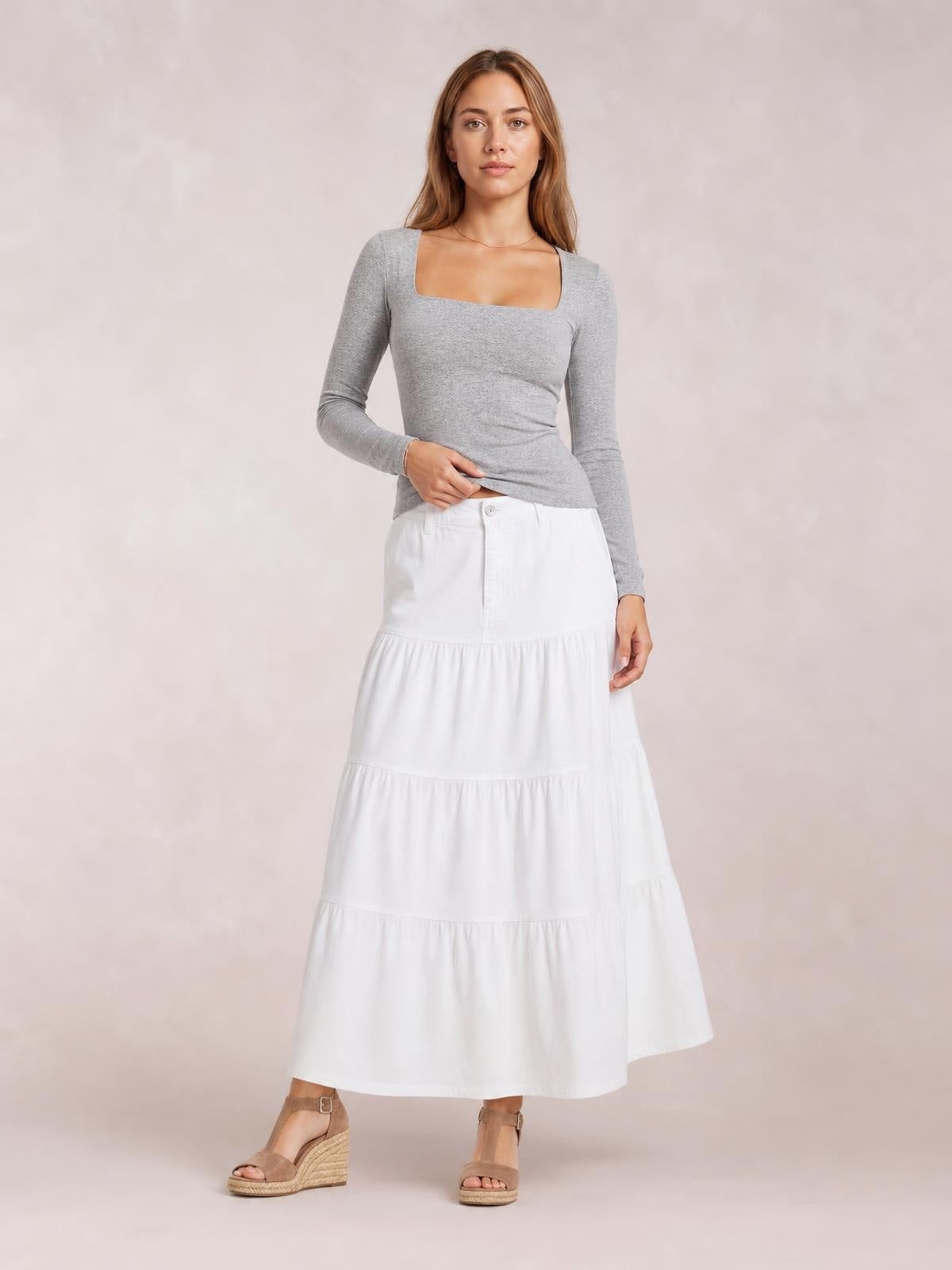 Model wearing a fitted gray square neck long sleeve T-shirt, shown front-facing with one hand lifting the hem to reveal its stretchy silhouette.