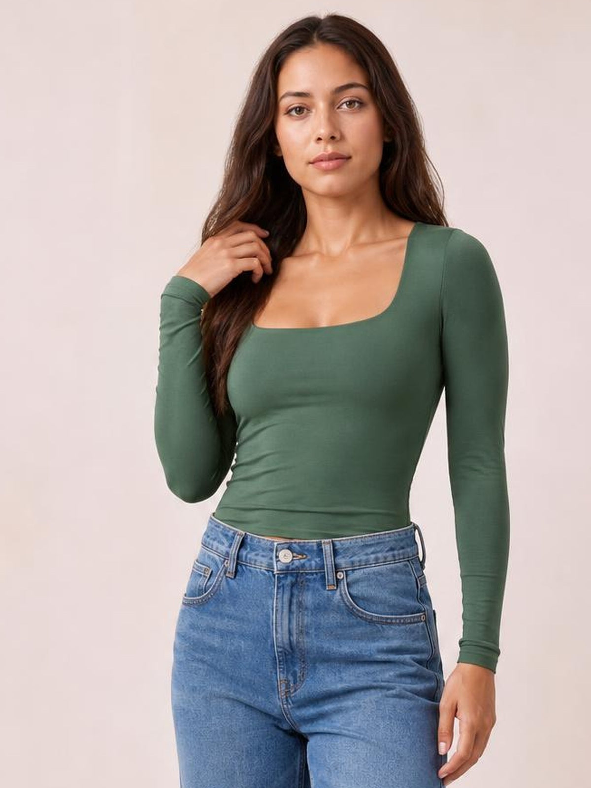 Model wearing a fitted forest green square neck long sleeve T-shirt with a smooth opaque finish, paired with jeans and touching her hair.
