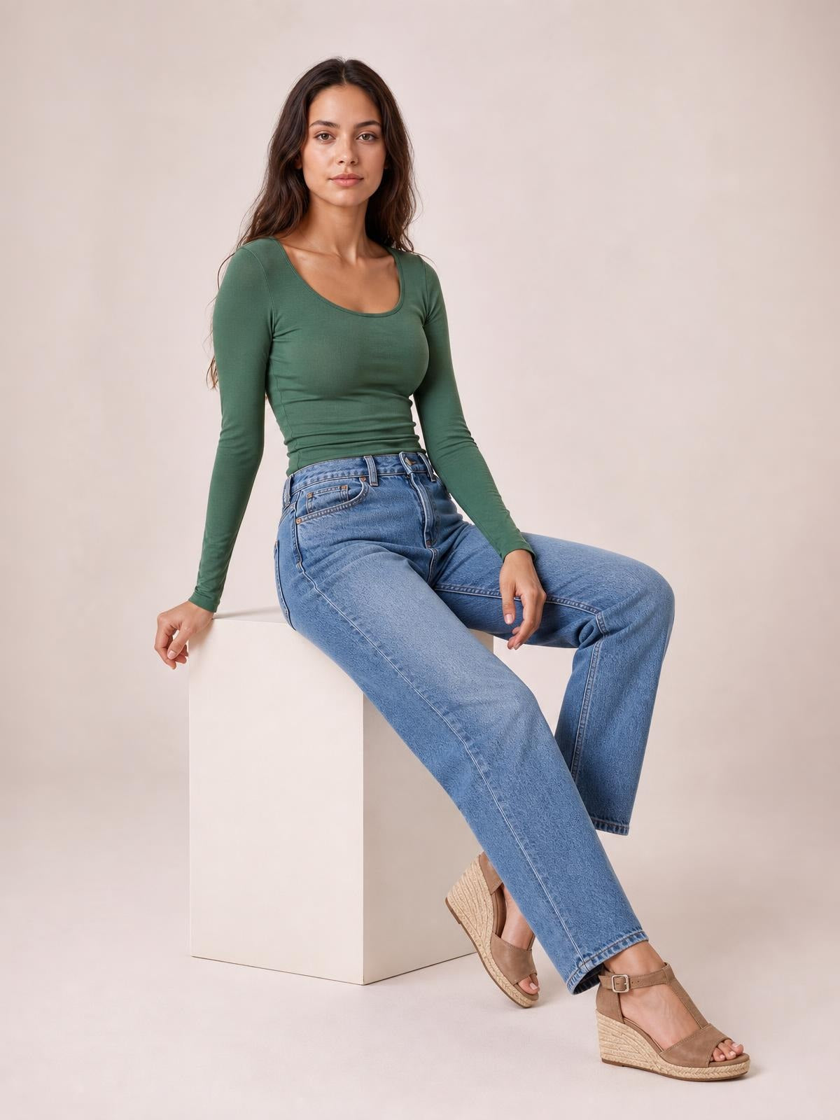 Model seated in a relaxed pose wears a fitted green long sleeve T-shirt with a wide square neckline and smooth, stretchy silhouette.