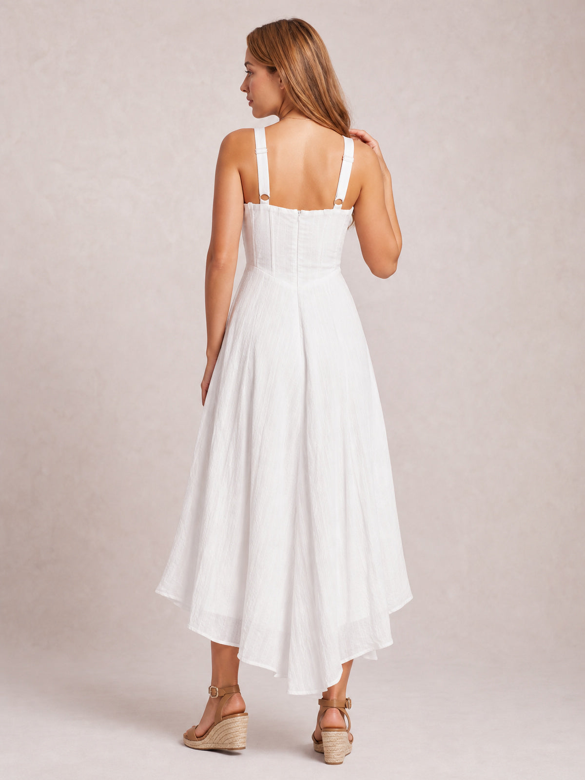 Back view of a model in a white midi cami dress with slim shoulder straps, fitted seamed bodice, visible back zipper, and a fluid full skirt.