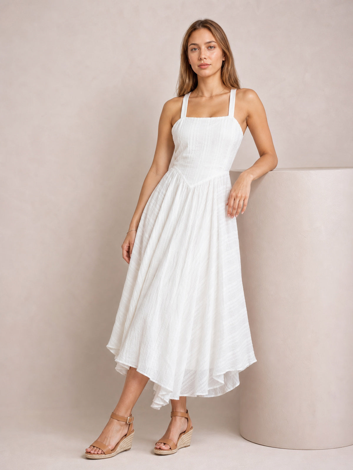 Model poses in a white square-neck midi cami dress with wide shoulder straps, a fitted textured bodice, defined waist, and flowing full skirt.