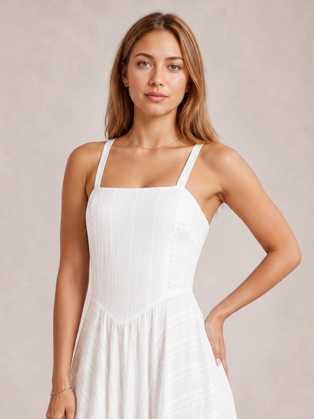 Model poses in a white square neck midi cami dress with slim straps, a fitted textured bodice, and a full fluid skirt, one hand resting on her hip.