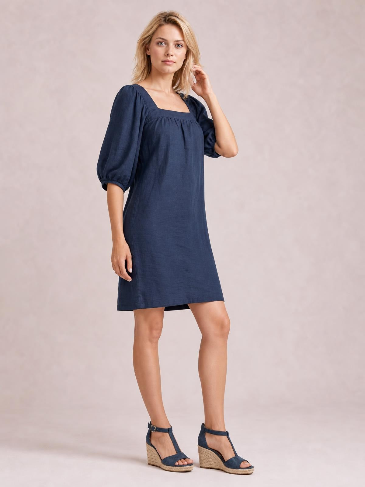 Model poses in a navy square-neck mini dress with voluminous puff sleeves, gathered seam detail, and a relaxed straight silhouette.