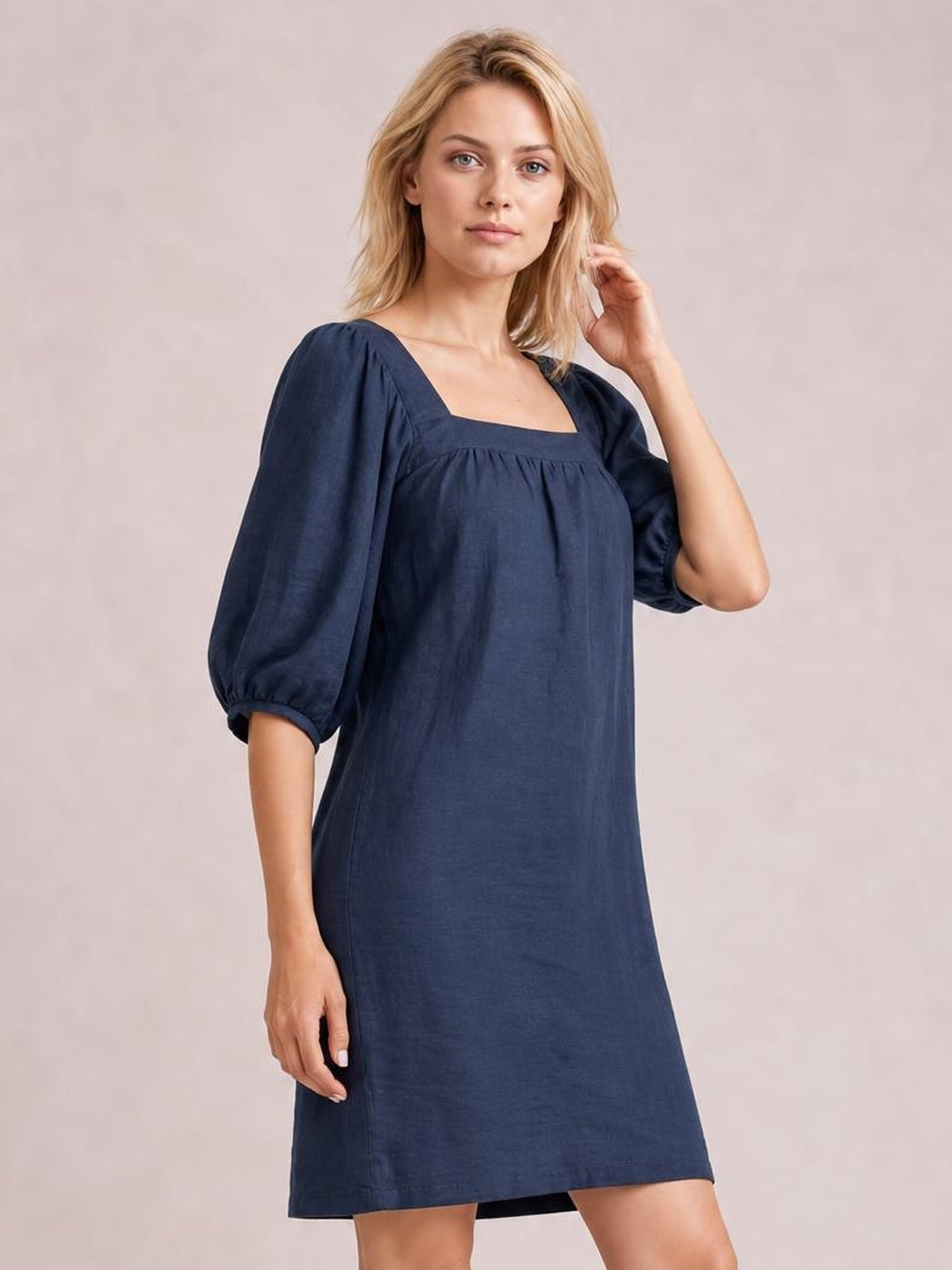 Model poses in a relaxed navy mini dress with a square neckline, gathered seam detail, voluminous puff sleeves, and a straight silhouette.