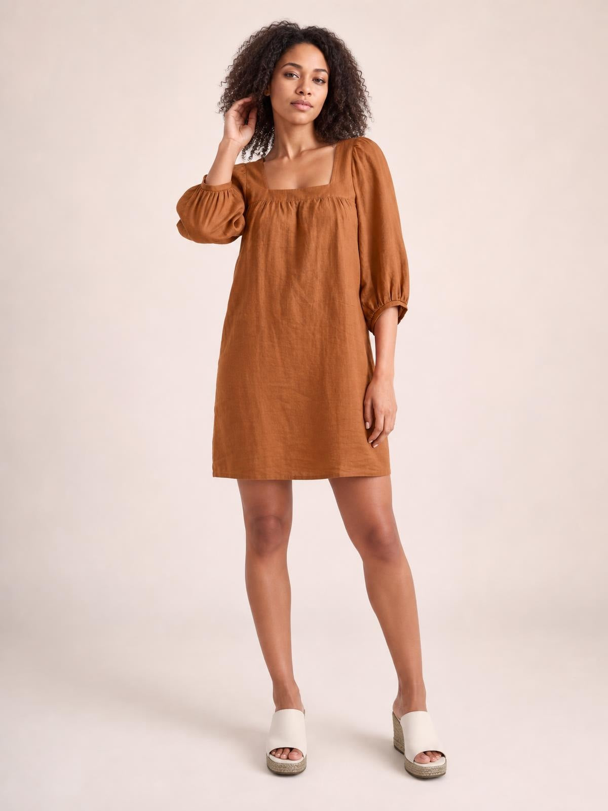 Model poses in a relaxed rust-brown mini dress with a square neckline, gathered puff sleeves, seam detailing, and a straight silhouette.