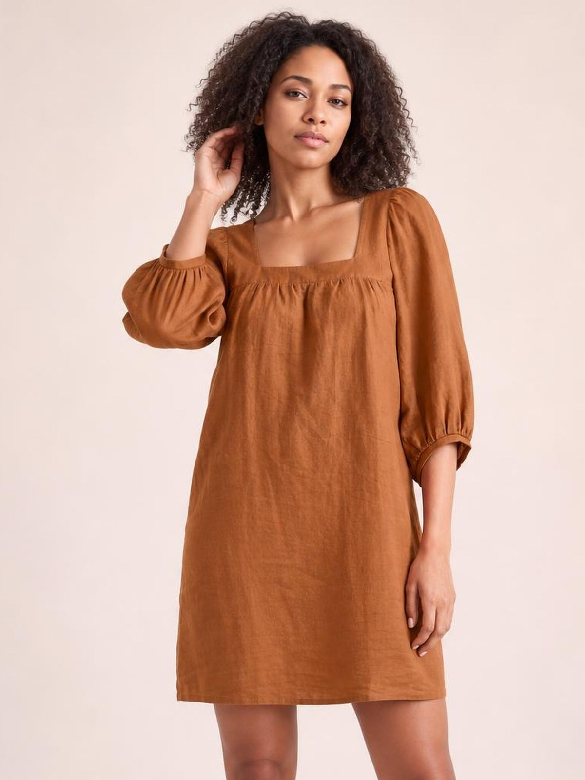Model poses in a relaxed-fit rust brown mini dress with a square neckline, gathered puff sleeves, seam detail, and straight silhouette.
