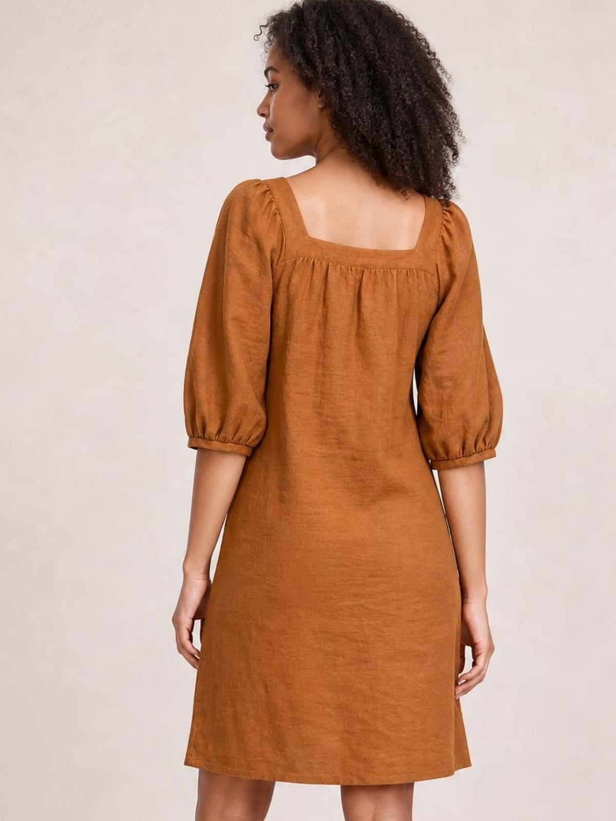 Model shown from the back wearing a rust-brown square neck mini dress with gathered puff sleeves, seam detailing, and a relaxed straight silhouette.