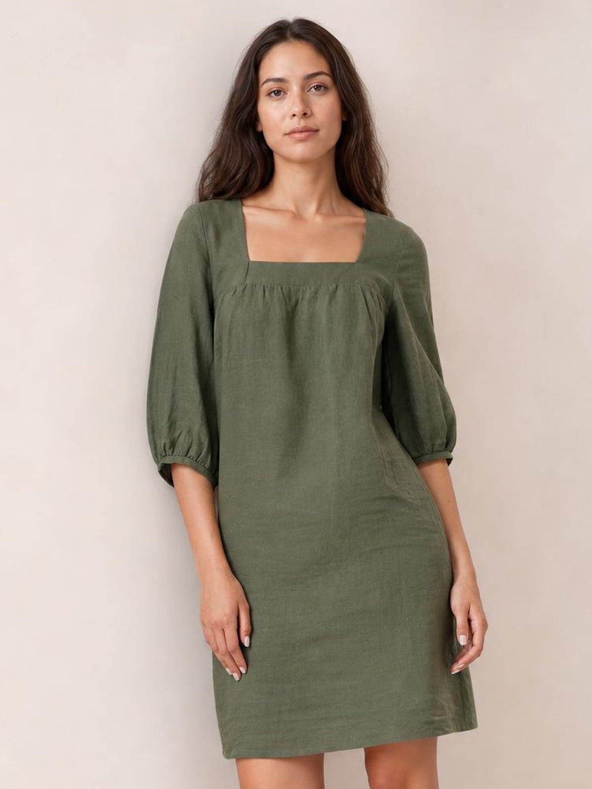 A model stands in an olive-green square neck mini dress with relaxed silhouette, gathered seam detail, and three-quarter puff sleeves with elastic cuffs.