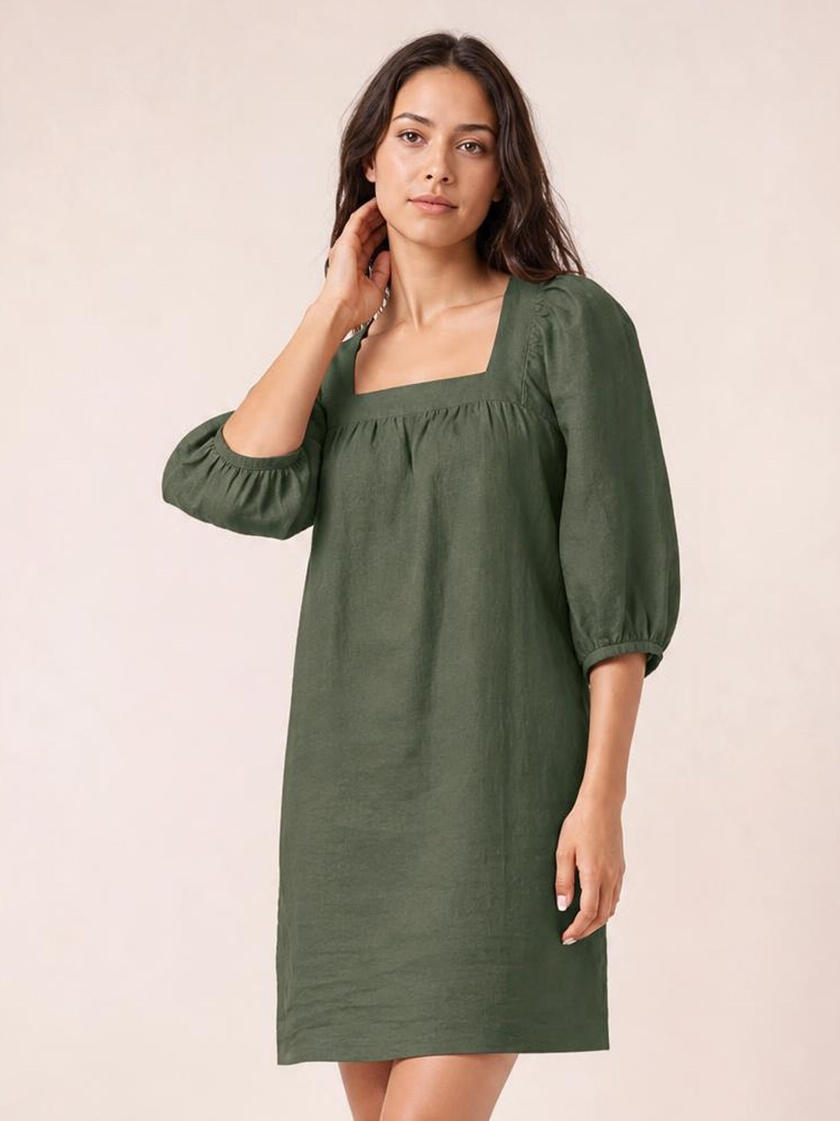 A model poses in an olive-green square neck mini dress with gathered puff sleeves, seam detailing, and a relaxed straight silhouette.