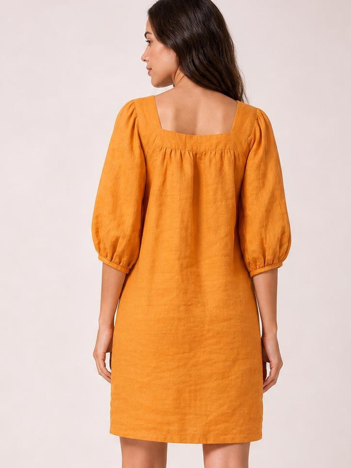 A model faces away in an orange square-neck mini dress with puff sleeves, seam detailing, and a relaxed straight silhouette.