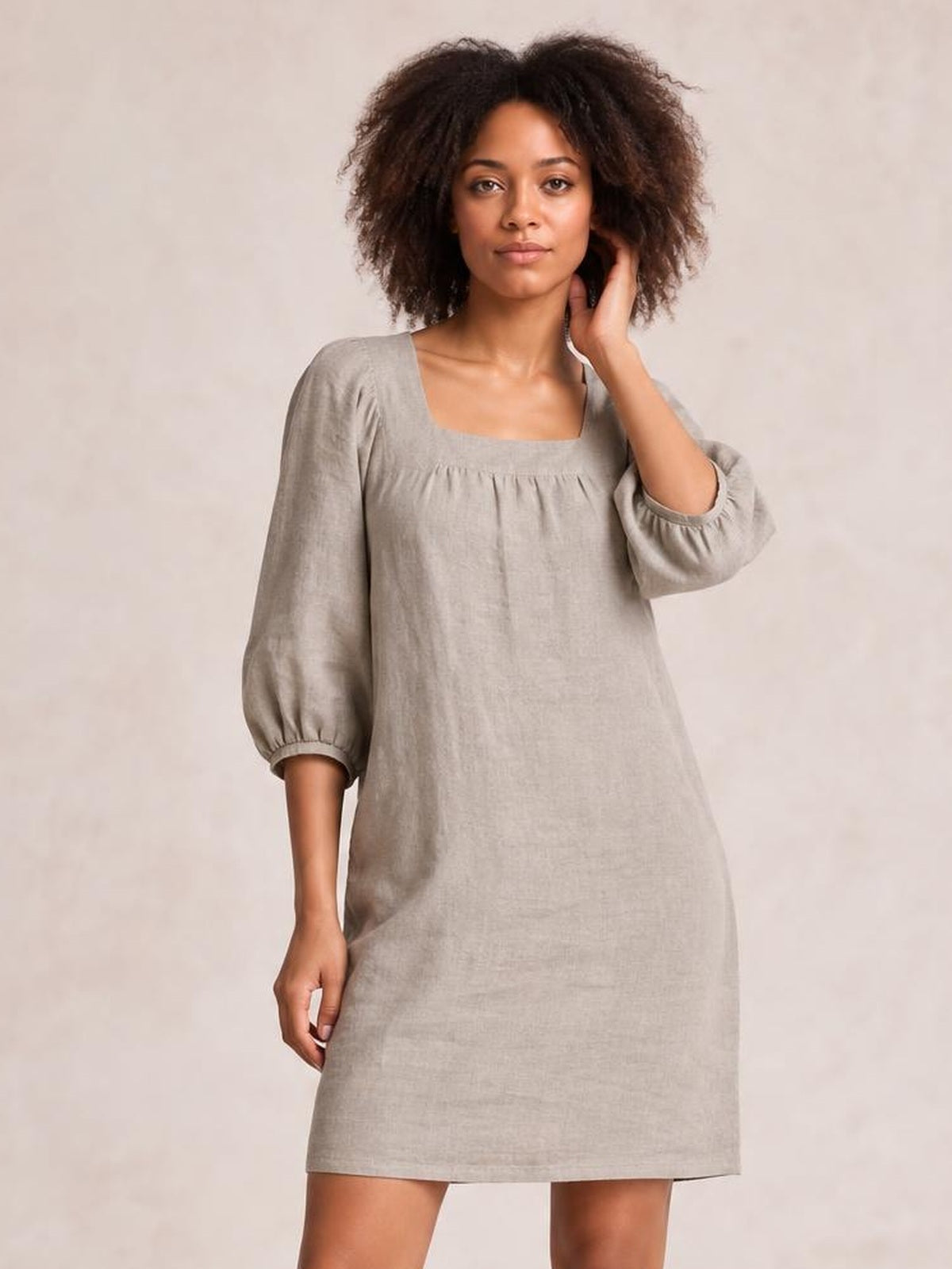 Model poses in a relaxed taupe mini dress with a square neckline, gathered puff sleeves, visible seam detail, and an easy A-line silhouette.
