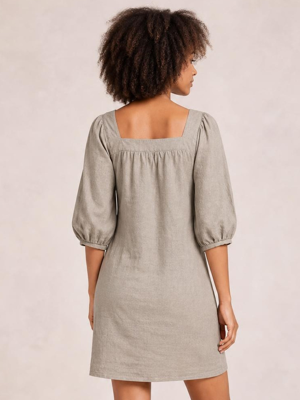 Model shown from behind wearing a taupe square-neck mini dress with puff sleeves, gathered seam detail, and a relaxed straight silhouette.