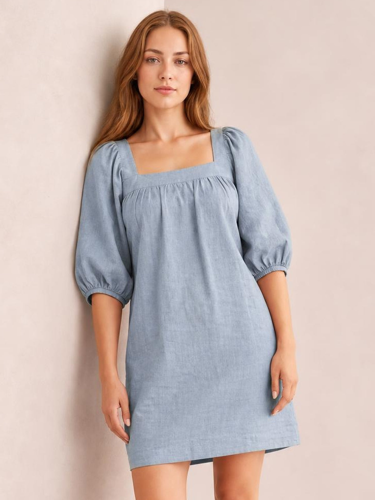 Model stands in a relaxed pose wearing a light blue square-neck mini dress with puff sleeves, gathered seam detail, and a straight silhouette.