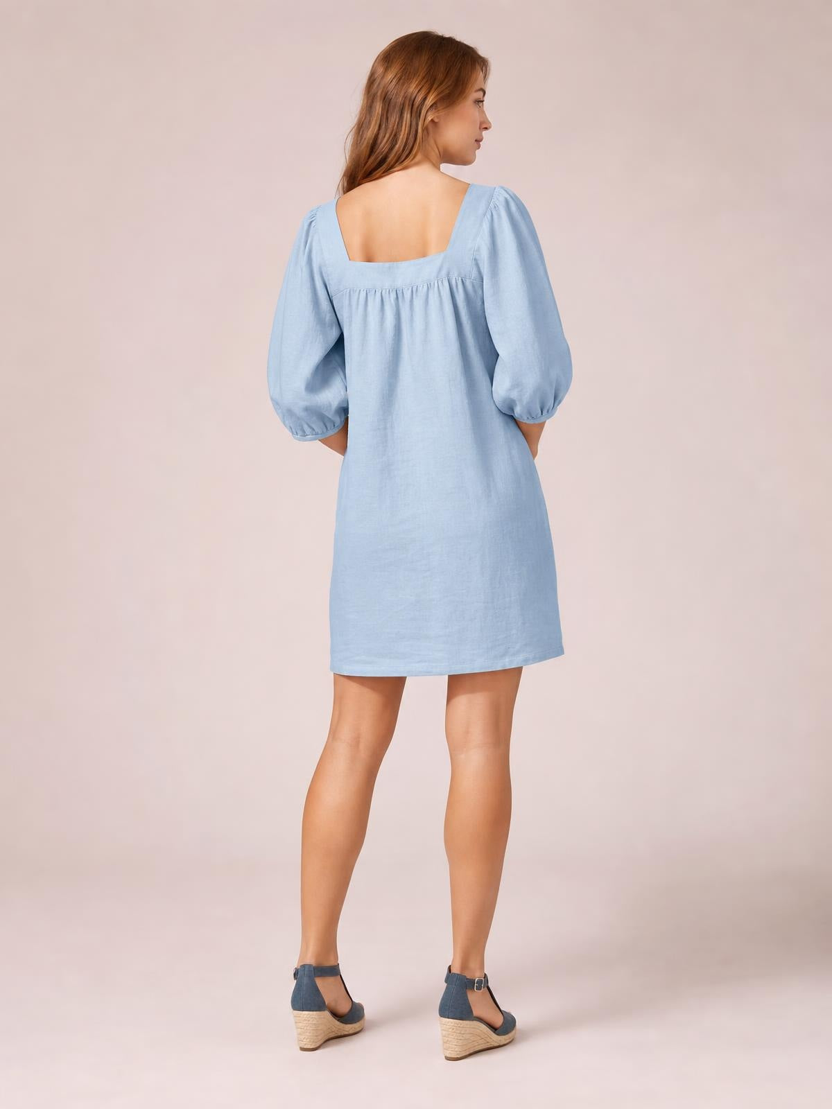 Model turned to show the back of a light blue square-neck mini dress with voluminous puff sleeves, seam detail, and a relaxed straight silhouette.
