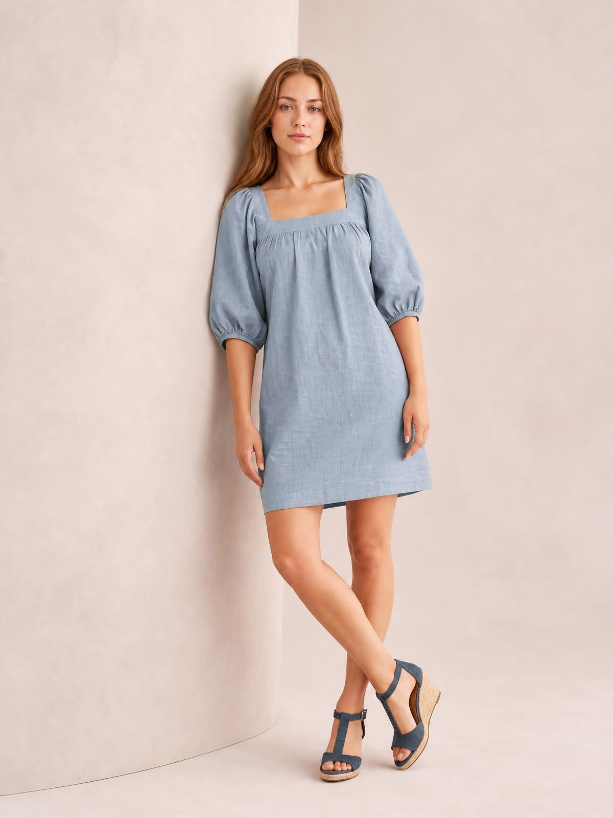 Model poses in a light blue square neck mini dress with puff sleeves, gathered seam detail, and a relaxed straight silhouette.