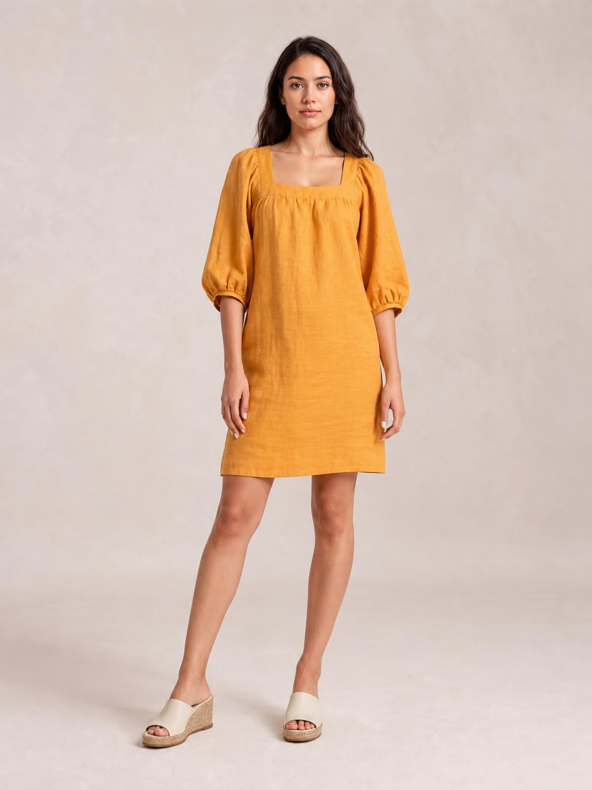 Model poses in a mustard yellow square neck puff sleeve mini dress with seam detailing and a relaxed, straight silhouette.