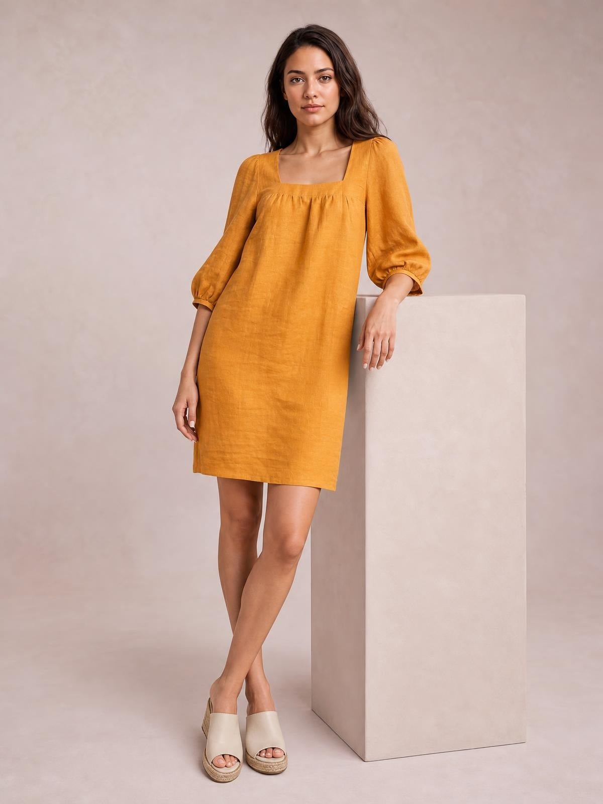 A model poses in a mustard square-neck mini dress with gathered puff sleeves, seam detailing, and a relaxed straight silhouette.