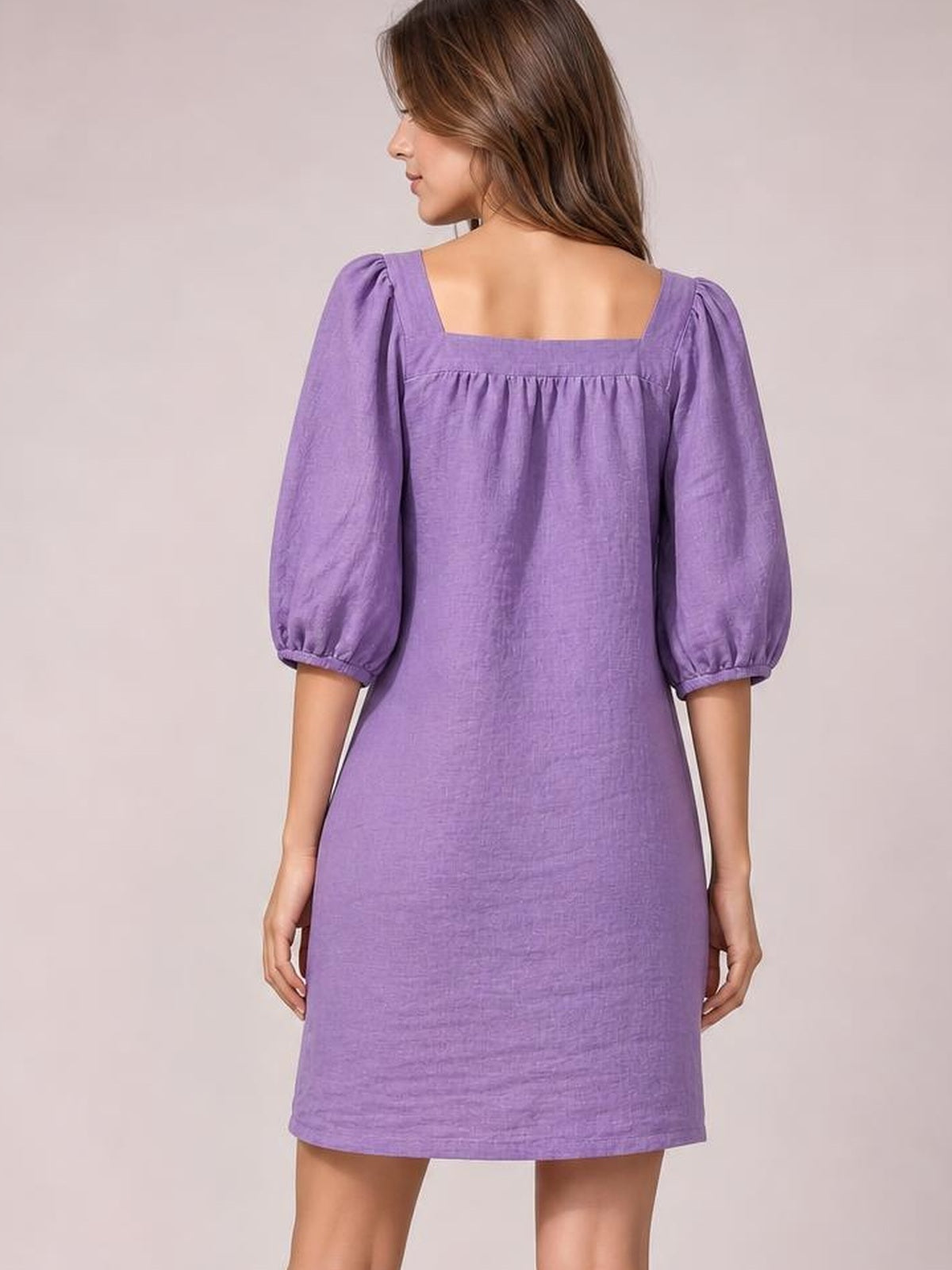 A model stands facing away in a relaxed purple mini dress with a square neckline, puff sleeves, gathered seam detail, and a straight silhouette.