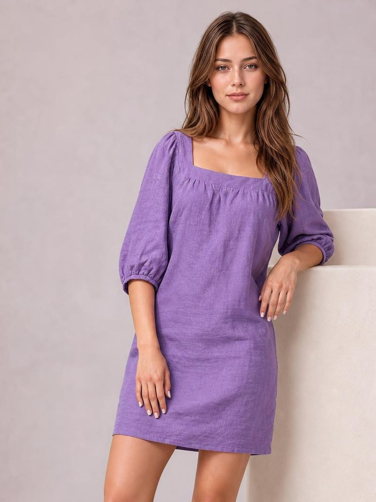 Model poses in a purple square-neck mini dress with puff sleeves, gathered seam detail, relaxed straight silhouette, and three-quarter elastic cuffs.