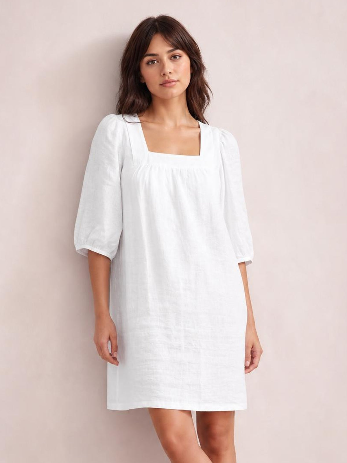 Model stands in a relaxed white mini dress with a square neckline, puff sleeves, visible seam detail, and an easy straight silhouette.