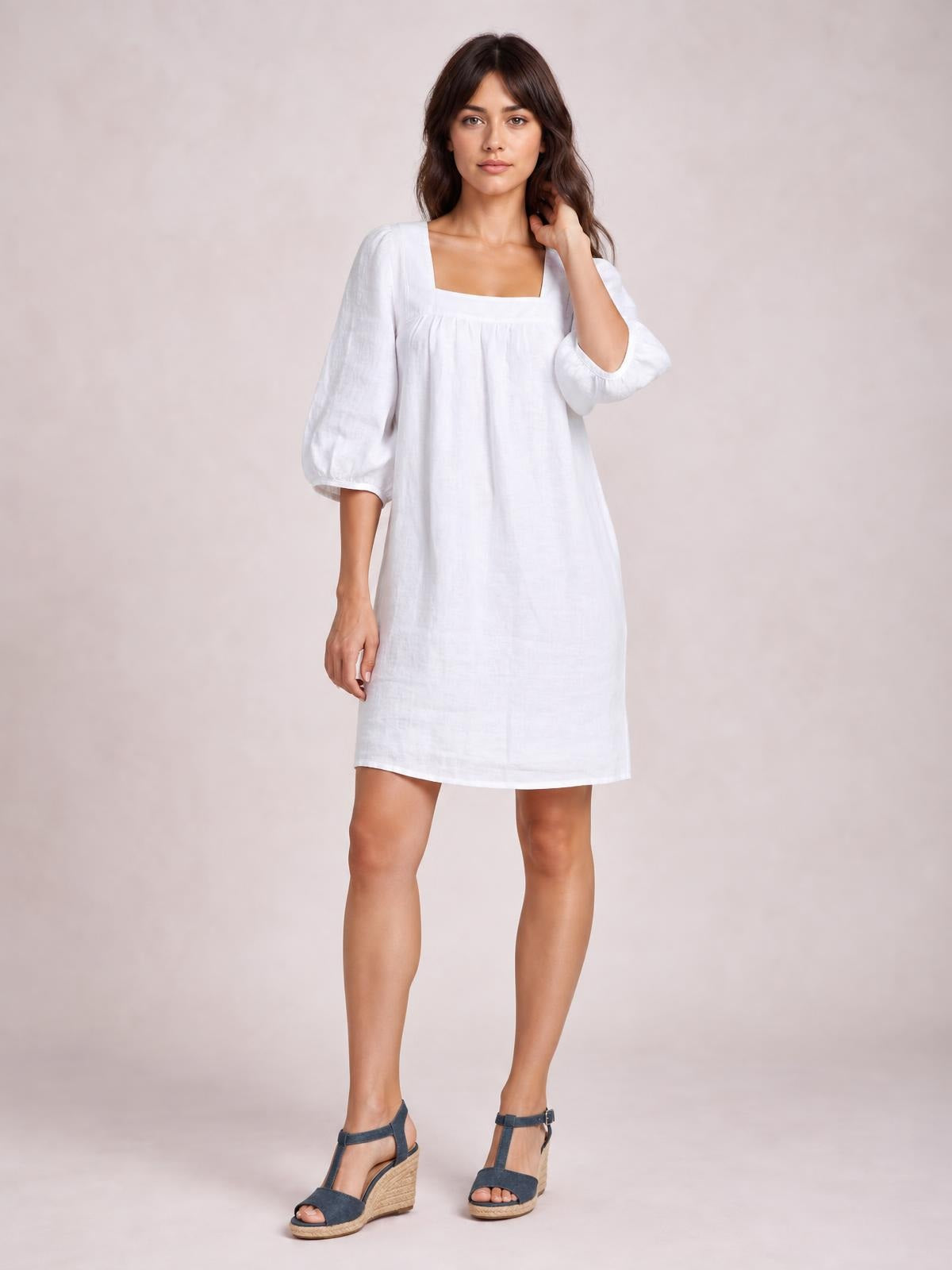 Model poses in a white square-neck mini dress with puff sleeves, seam detailing, and a relaxed straight silhouette.