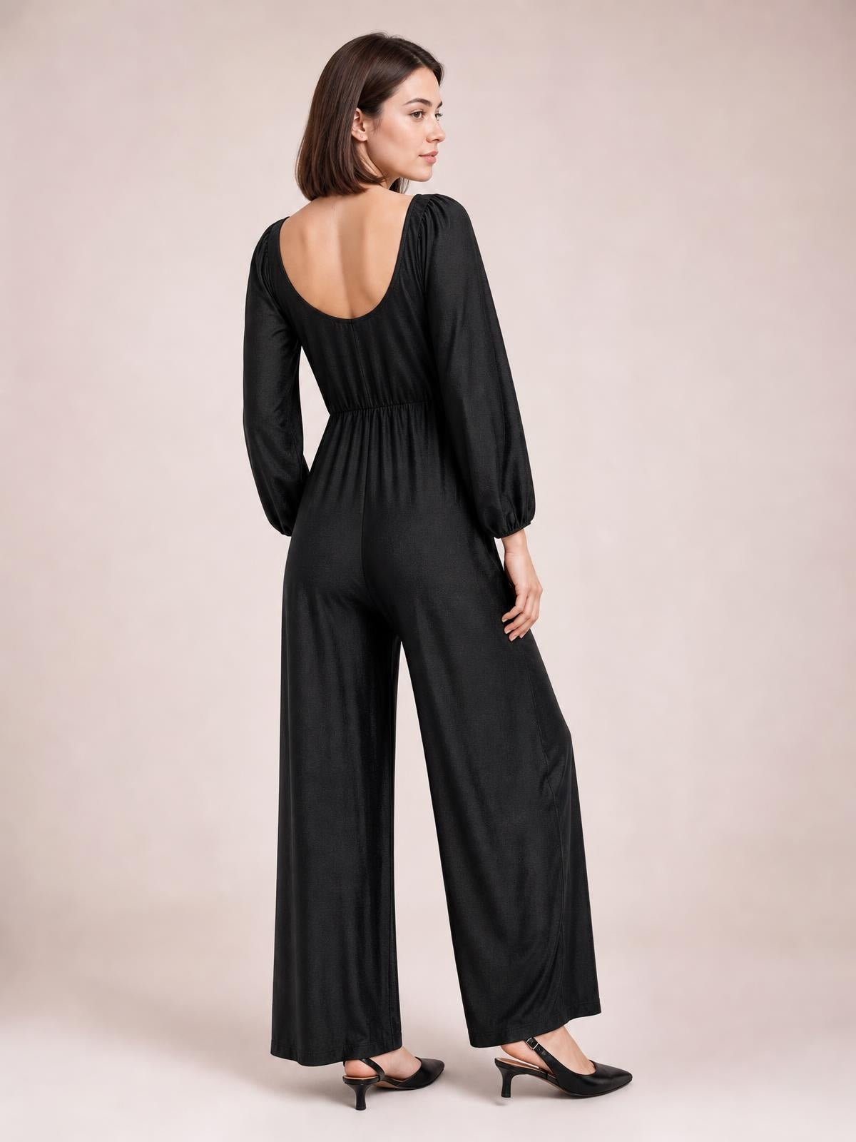 Model shown from the back in a solid black jumpsuit with long raglan sleeves, a low square neckline, gathered waist, and wide-leg silhouette.