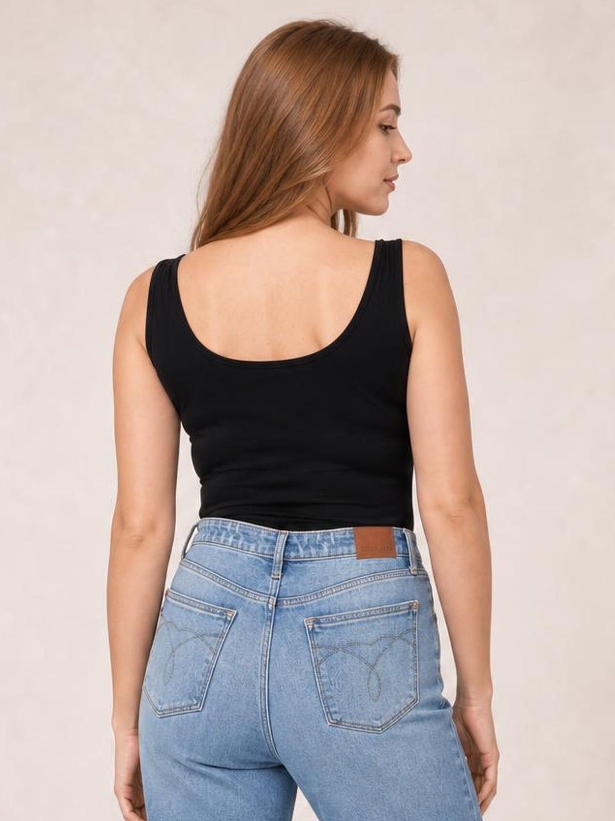A model looks over her shoulder, showing a black sleeveless bodysuit with a rounded back neckline and close-fitting, slightly stretchy silhouette.