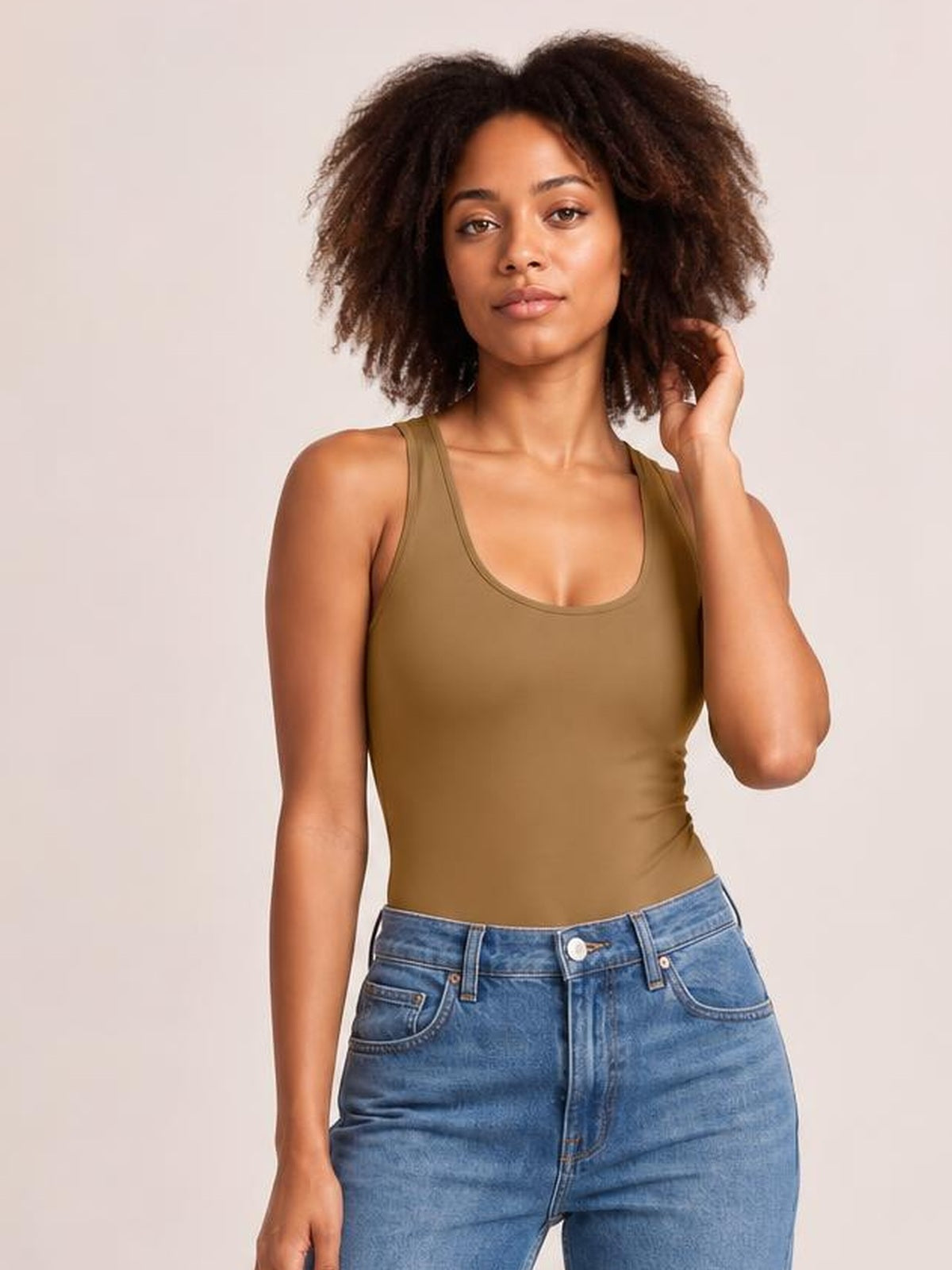 Model poses in blue jeans and an olive square neck sleeveless bodysuit with a fitted silhouette, wide shoulder straps, and slight stretch.