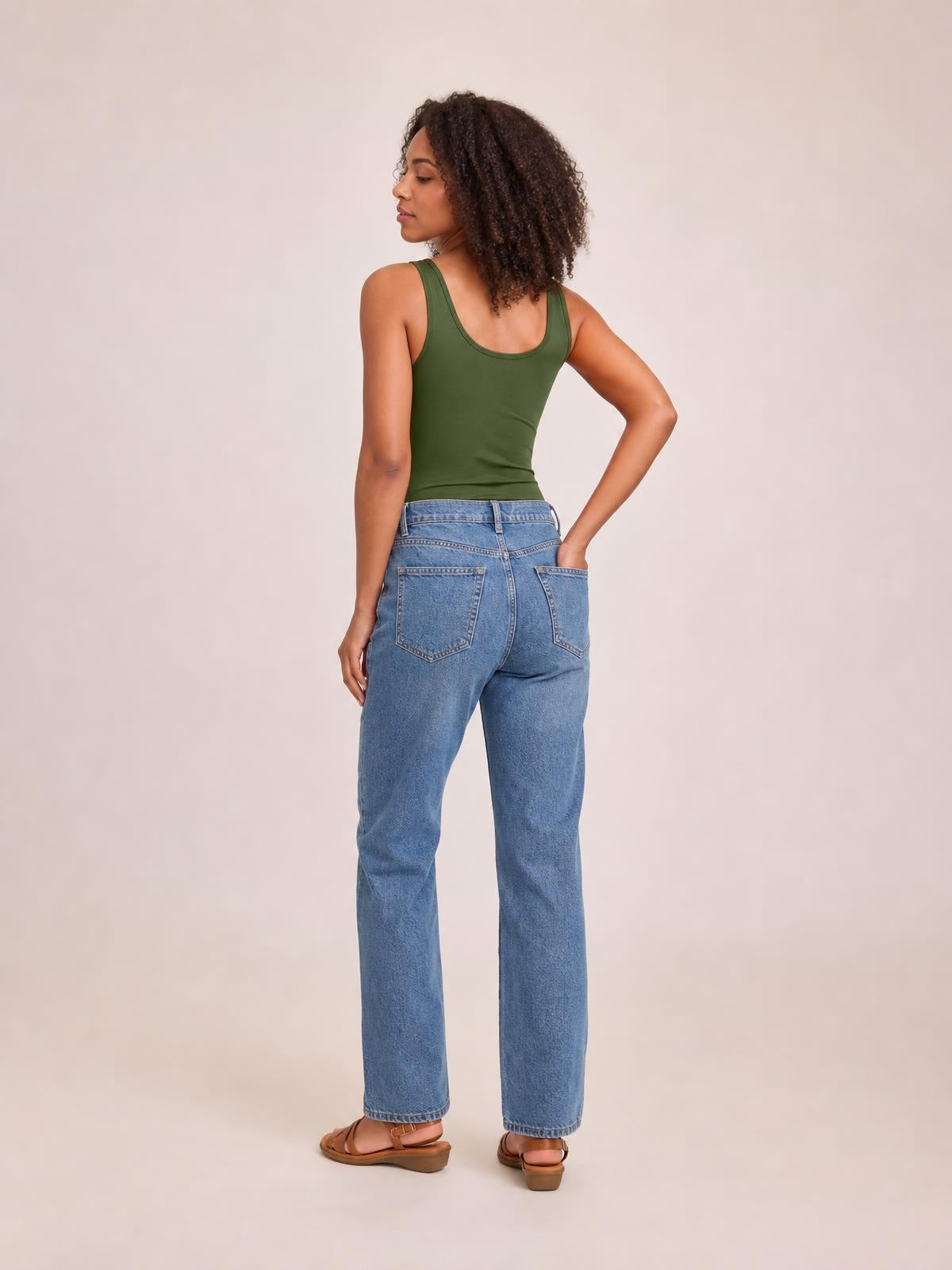A model poses from the back in a fitted olive green sleeveless bodysuit with wide straps and a smooth, lightly stretchy silhouette.