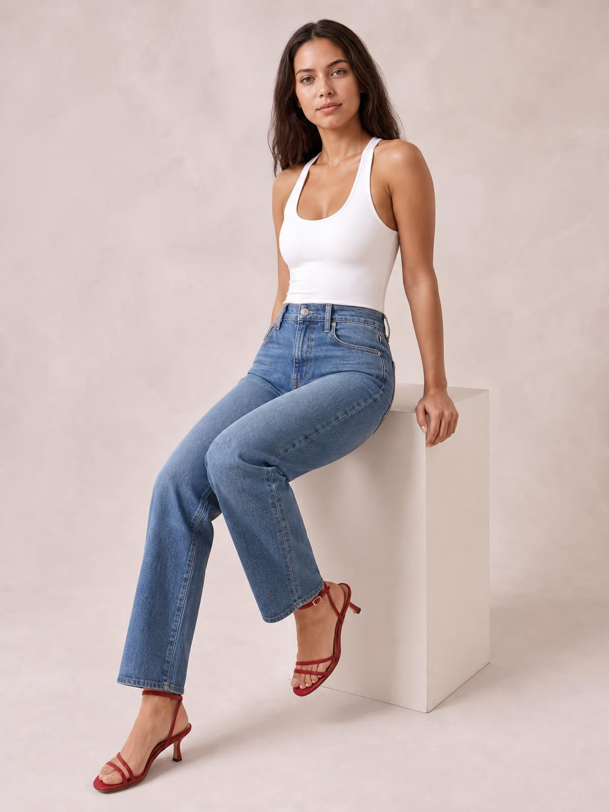 A model sits in a fitted white square-neck sleeveless bodysuit with slim straps and a smooth, close-fitting silhouette.