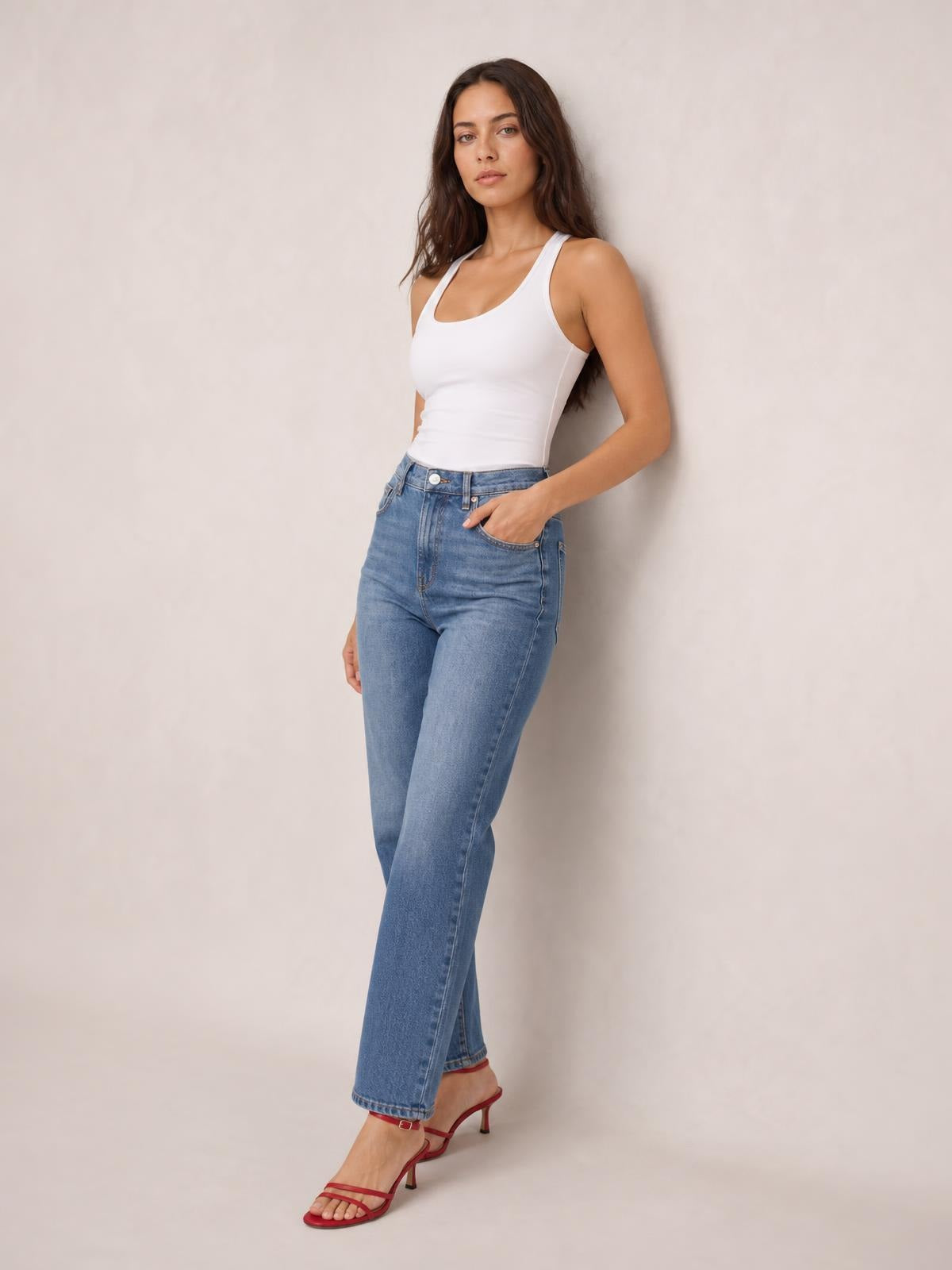Model wears a white square-neck sleeveless bodysuit with a fitted silhouette and slight stretch, standing with one hand in her jeans pocket.