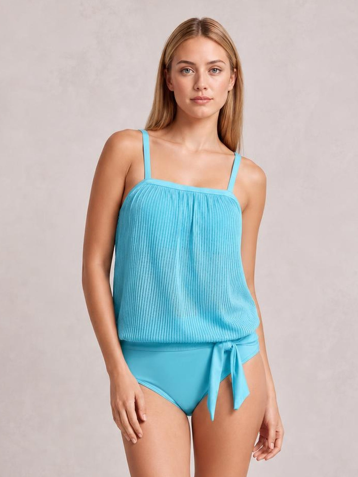 Model stands in a turquoise square-neck spaghetti-strap tankini set with a textured relaxed silhouette, attached shorts, and a front waist tie.