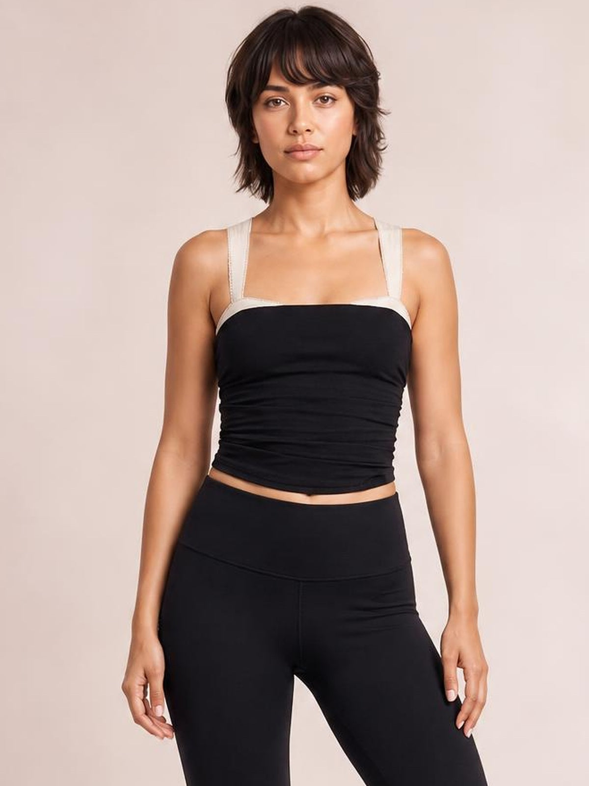Model standing in a black square neck wide strap cami with a fitted, slightly ruched silhouette and cropped hem.