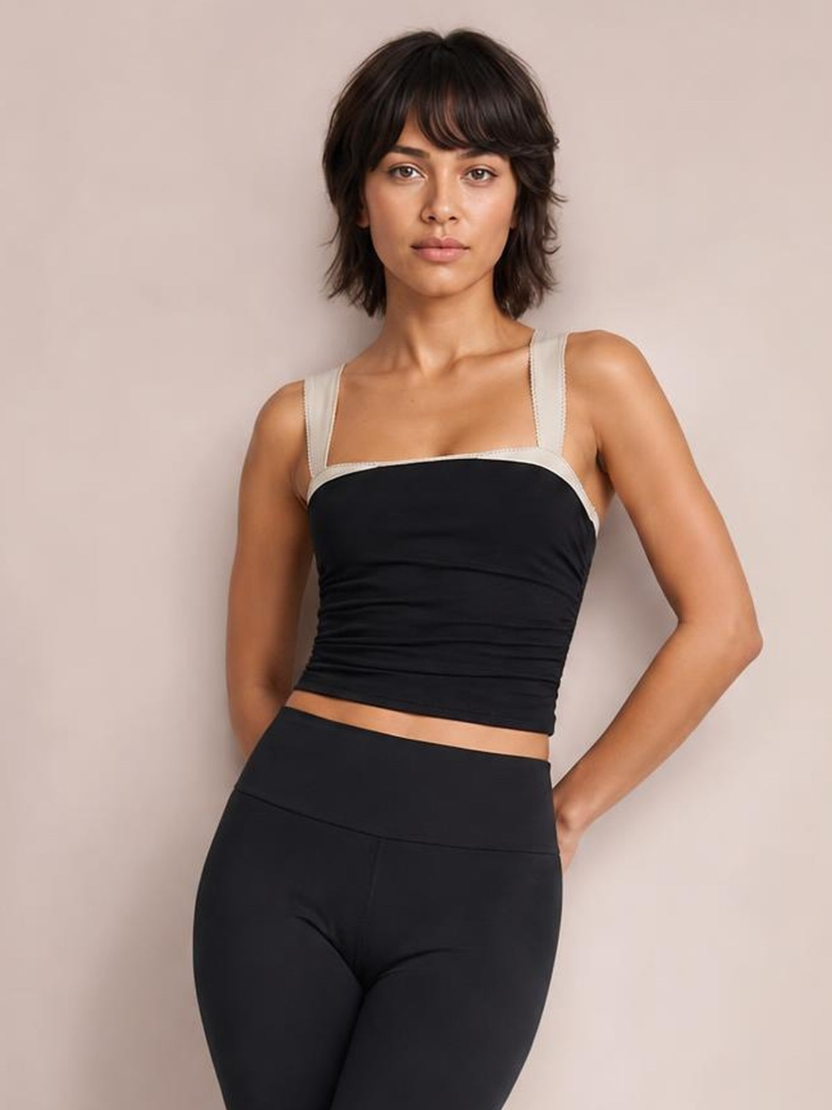 Model poses with one hand on her hip wearing a black square-neck cami with wide straps and a fitted, slightly ruched silhouette.