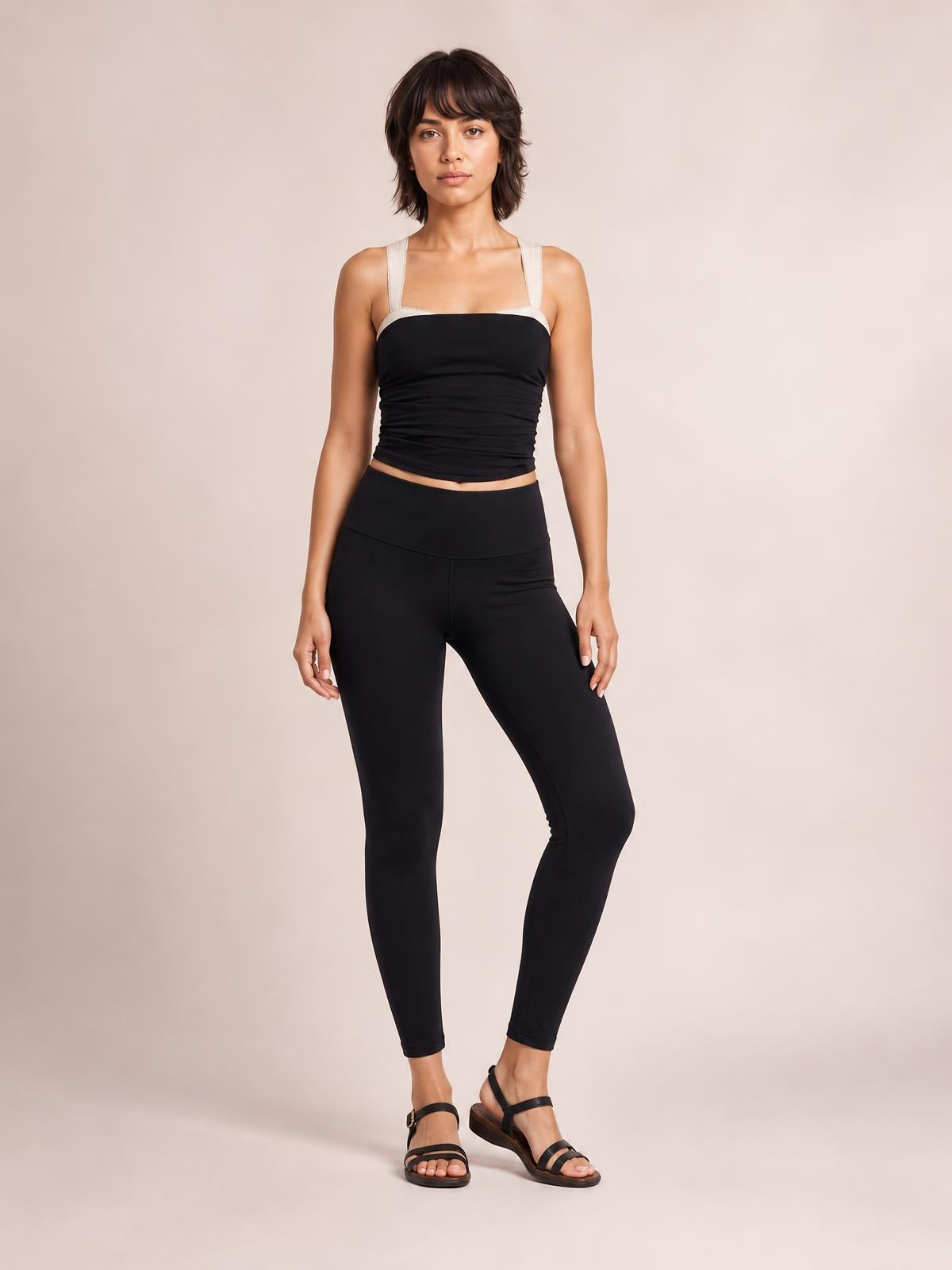 A model stands with one knee bent wearing a black square-neck wide-strap cami with a fitted, slightly cropped silhouette.