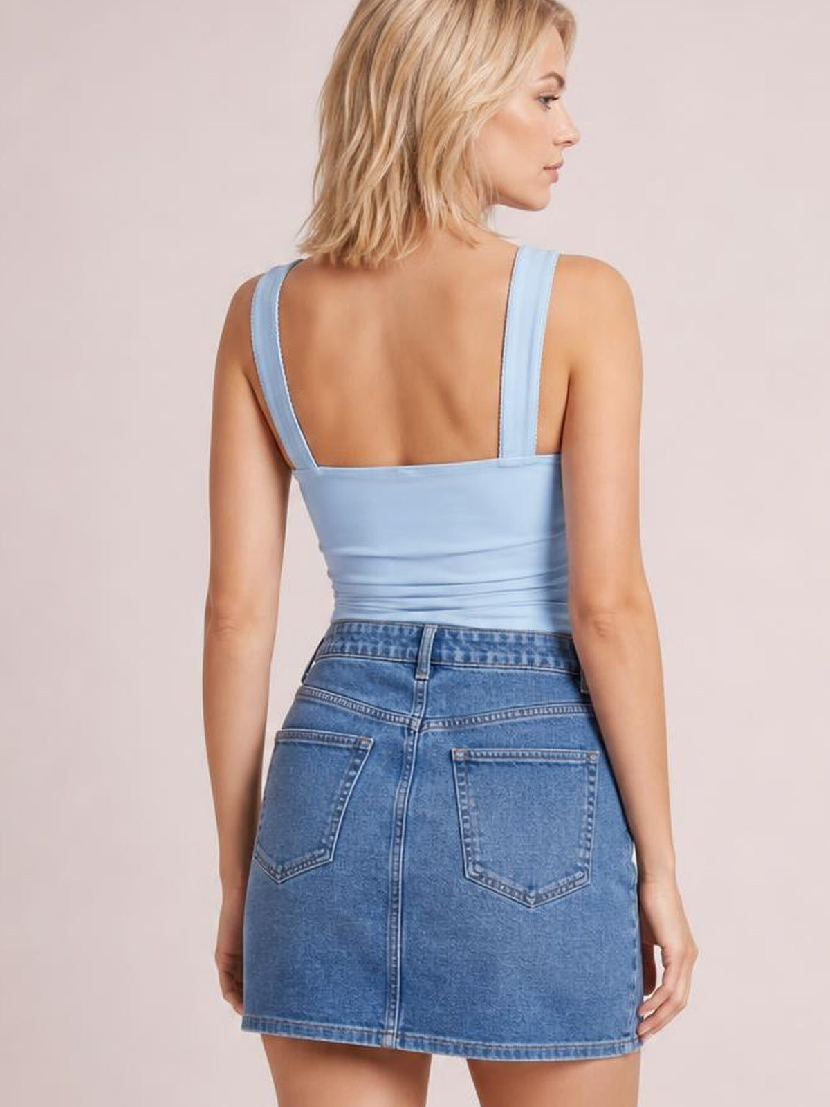 Back view of a model wearing a light blue square neck cami with wide straps, a fitted silhouette, and subtle waist ruching.