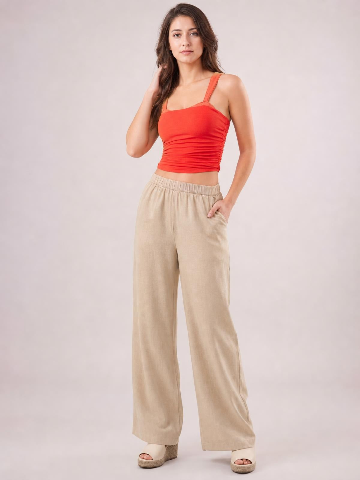 Model wearing a red square neck cami with wide straps, ruched sides, and a fitted cropped silhouette, posing with one hand in her pocket.