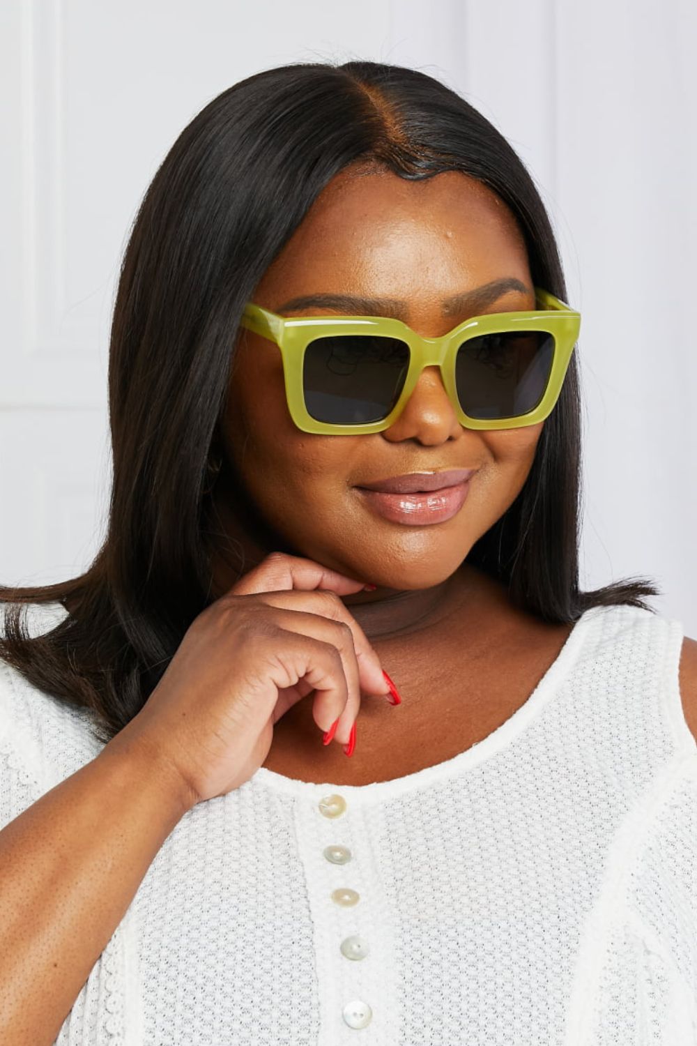 Model poses with one hand under her chin, wearing bold square sunglasses with a vivid neon yellow acetate frame and dark TAC polarized lenses.
