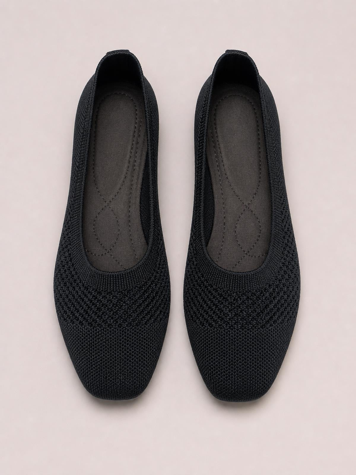 Pair of black solid-color mesh slip-ons shown from above, featuring square toes, flat silhouettes, cushioned stitched insoles, and flexible rubber soles.