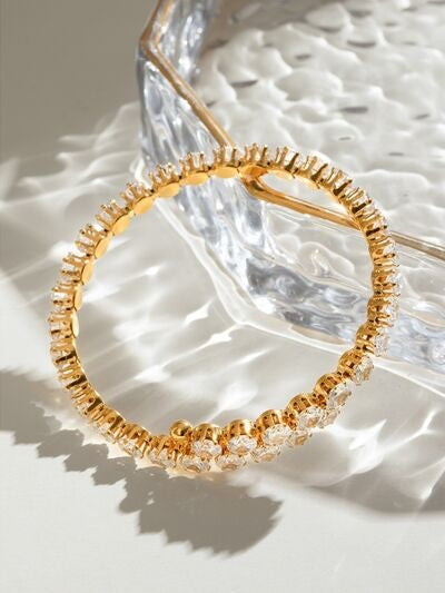 A gold-tone stainless steel bangle bracelet features a slim circular silhouette with ridged construction and sparkling clear zircon accents along the band.
