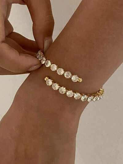 A hand adjusts an 18K gold-plated stainless steel inlaid zircon bracelet on a wrist, featuring a sparkling row of round stones and gold-tone ends.