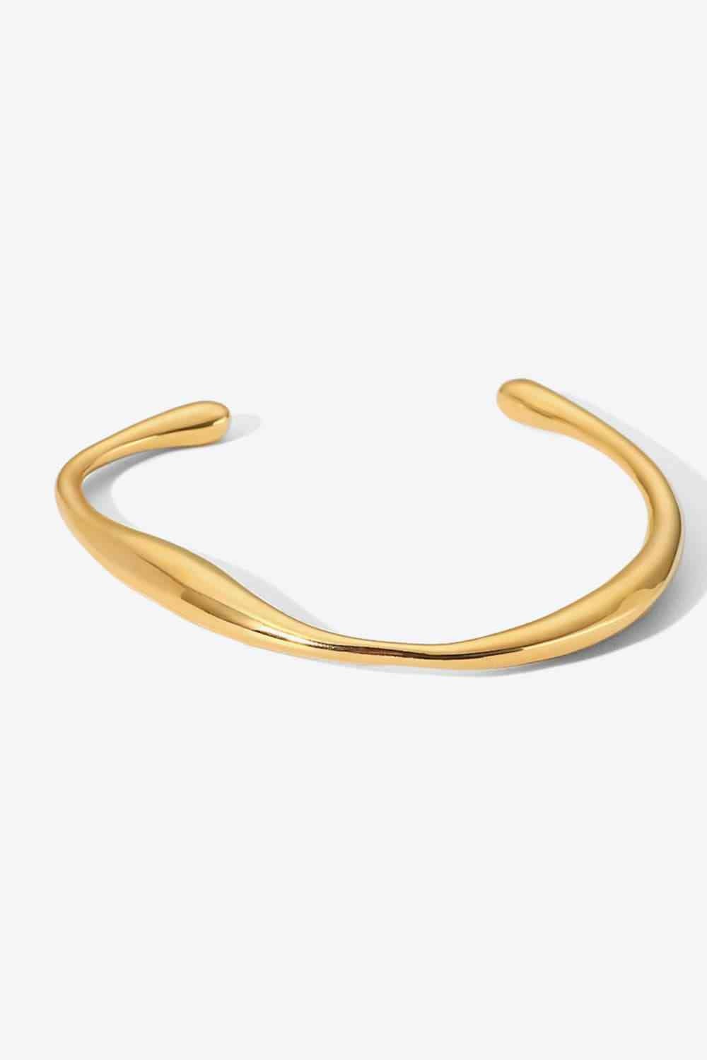 A modern 18K gold-plated stainless steel open bracelet features a smooth, polished curved band with rounded, tapered ends.
