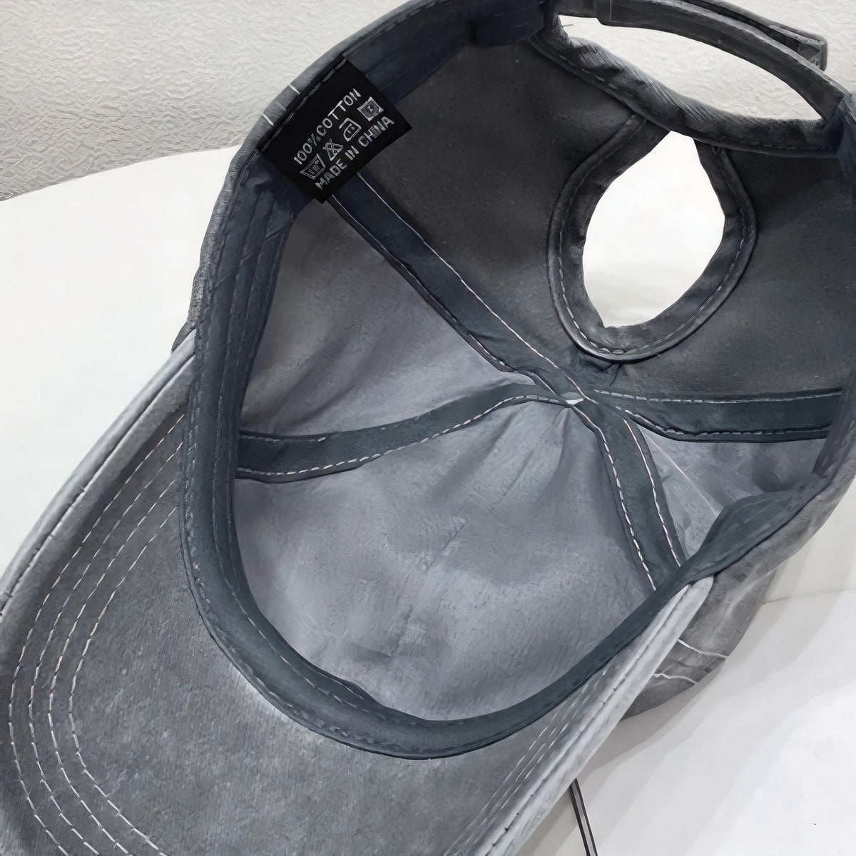 Inside view of a black cotton adjustable baseball cap showing the softly structured six-panel crown, stitched seams, curved brim, and back strap.