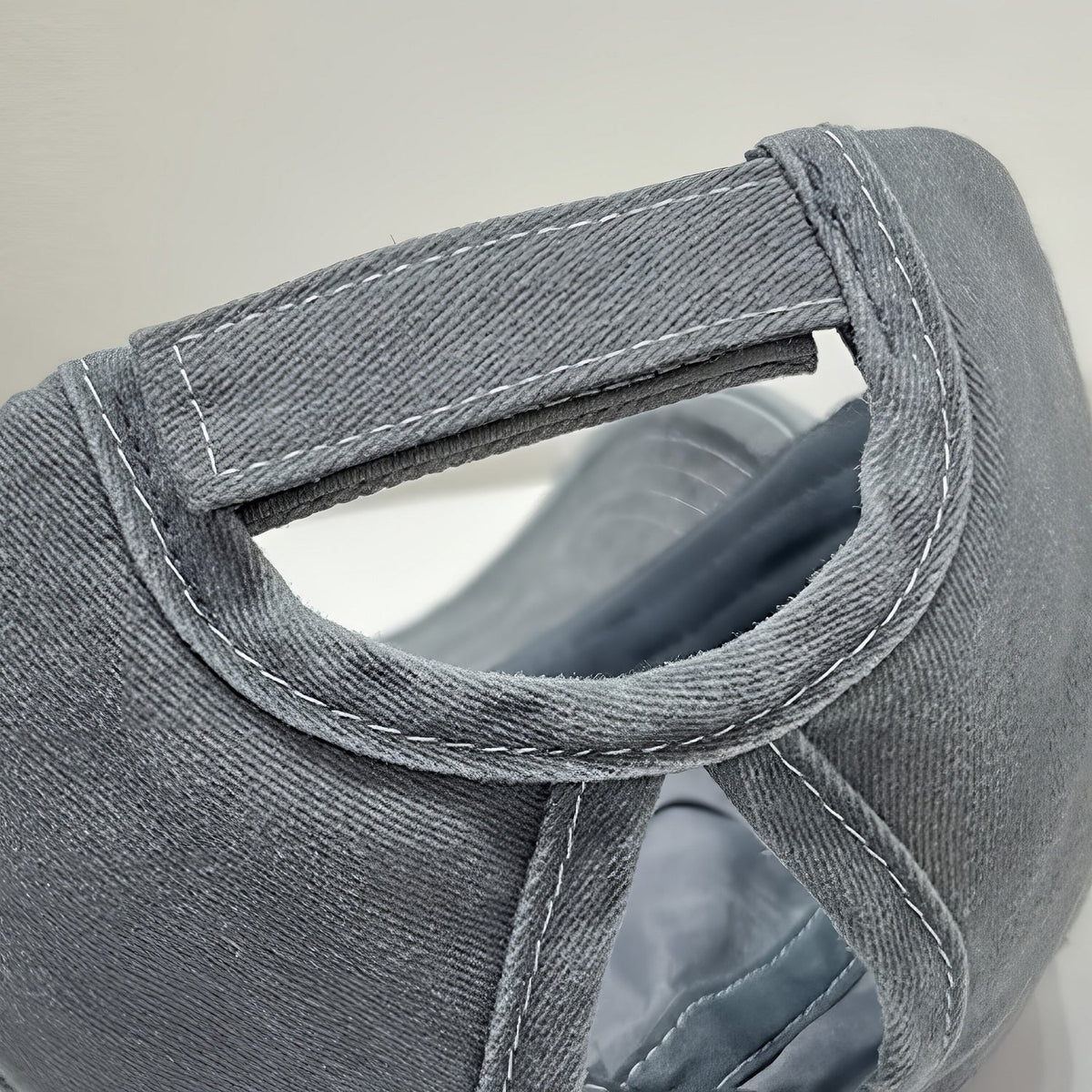 Close-up of the gray cotton baseball cap showing its six-panel construction, curved brim, contrasting white stitching, and adjustable back strap.