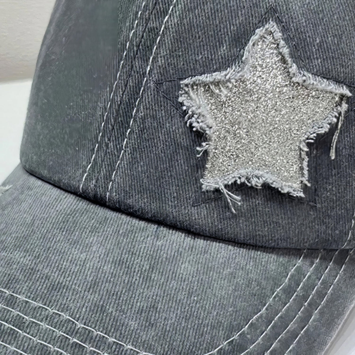 Close-up of a charcoal cotton baseball cap with a six-panel crown, curved brim, visible seams, distressed edging, and a textured star appliqué.